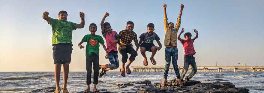boy wearing green crew neck shirt jumping from black stone on seashore